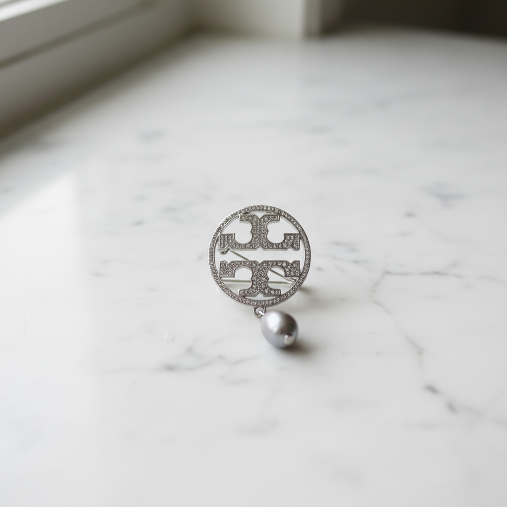 Tory Burch Miller Silver Pave Brooch on marble surface, editorial lifestyle shot