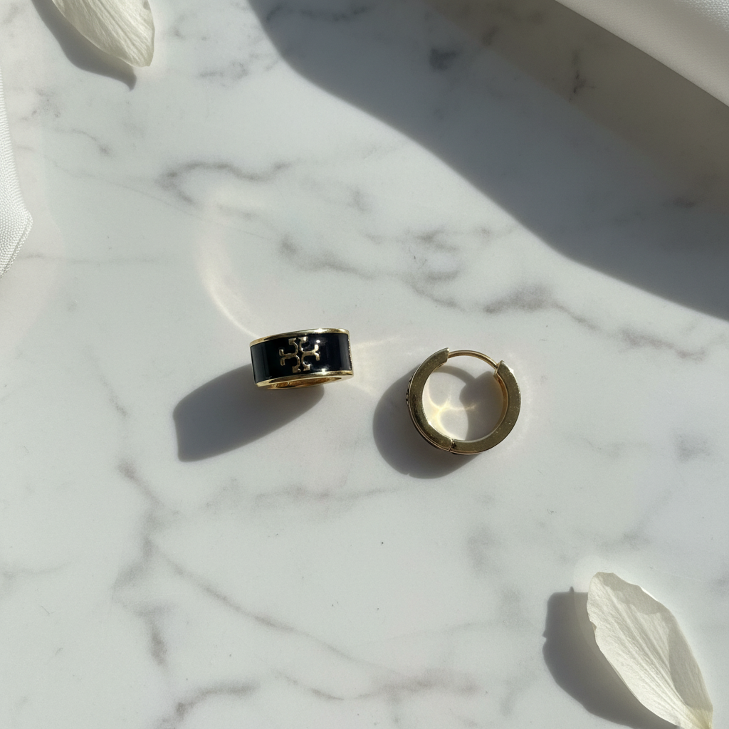 Tory Burch black enamel huggie earrings flat lay on white marble